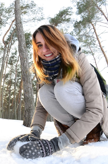 Een jong en vrolijk Kaukasisch meisje in een bruine jas beeldhouwt de sneeuw