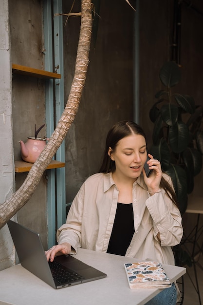 Een jong Europees freelancer-meisje met lang donker haar in een shirt en spijkerbroek werkt op afstand in een café