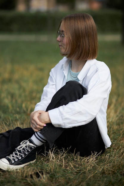 Een jong Europees meisje met een bril rust in een park op een groene staaf. Portret van een meisje