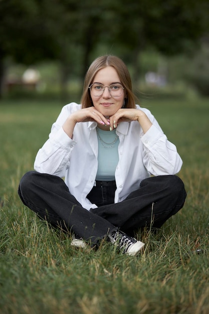 Een jong Europees meisje met een bril rust in een park op een groene staaf. Portret van een meisje