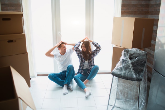 Een jong getrouwd stel in de woonkamer van het huis zit bij het raam. ze zijn blij met een nieuw huis. Verhuizen, kopen van een huis, appartement concept.