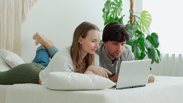 Een jong getrouwd stel ligt thuis op bed en gebruikt een laptop en bespreekt urgente kwesties.