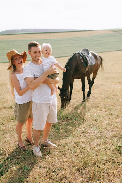 Een jong gezin heeft plezier in het veld. Ouders en kind met een paard