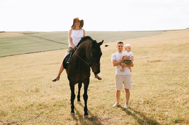 Een jong gezin heeft plezier in het veld. Ouders en kind met een paard