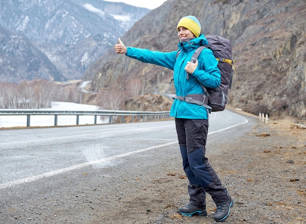 Een jong glimlachend meisje reist in de bergen stopt de auto op de weg liftend steekt zijn hand op