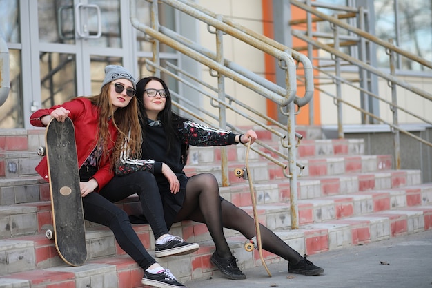 Een jong hipstermeisje berijdt een skateboard. Meisjes vriendinnen voor een wandeling in de stad met een skateboard. Lente sporten op straat met een skateboard.