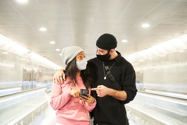 Een jong interraciaal stel geliefden met maskers en wollen hoeden loopt door een gang van de metro