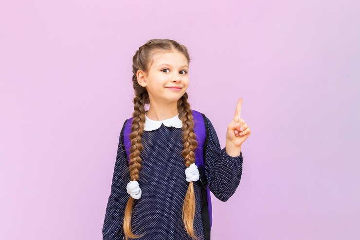 Een jong, jong schoolmeisje in een polkadot-jurk en met lange staartjes is erg blij en lacht