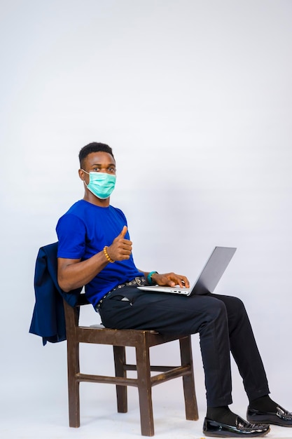 Een jong, knap afrikaans bedrijf geïsoleerd op een witte achtergrond met een gezichtsmasker om de uitbraak in de samenleving te voorkomen en voelt zich opgewonden over wat hij op zijn laptop zag