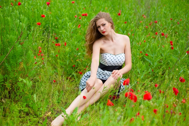 Een jong langharig meisje geniet van de kleuren van de natuur op een bloeiende papaverveld op een hete zomerdag.