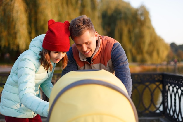 Een jong liefdevol gezin loopt langs het meer met een kinderwagen glimlachend ouderspaar met een babykinderwagen erin