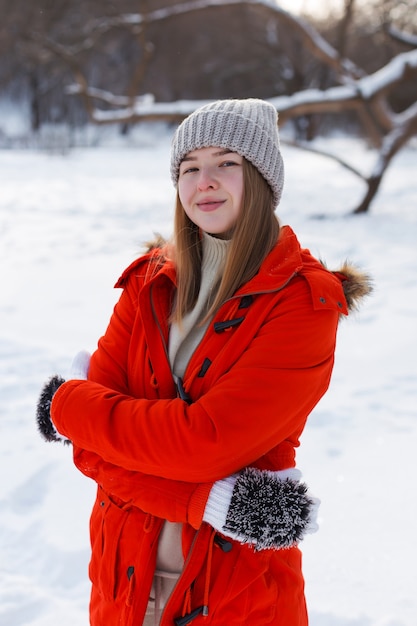 Een jong meisje, blond, in een trui, een hoed en een oranje jasje, tegen de achtergrond van het winterlandschap. sneeuw en vorst, het concept van kerstmis.