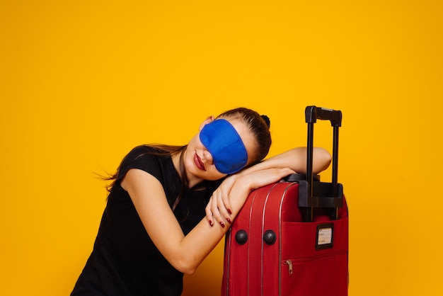 Een jong meisje gaat op reis, slapend op een grote rode koffer, voor een masker om te slapen