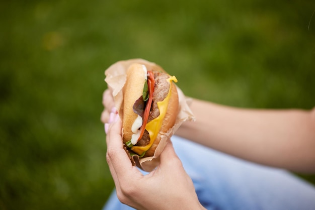 Een jong meisje haalt een hamburger uit een papieren zak die op het groene gras zit, het concept van straatvoedsel voor voedselbezorging