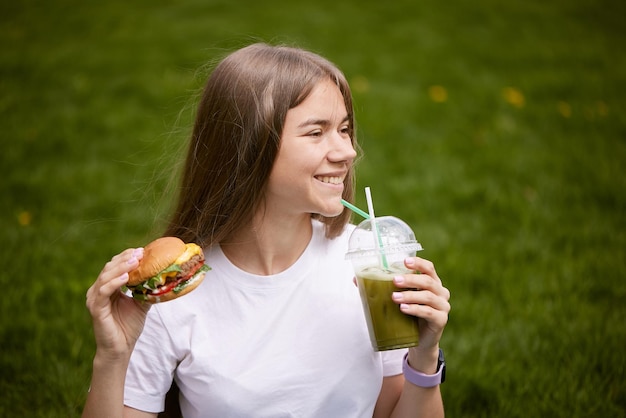 Foto een jong meisje haalt een hamburger uit een papieren zak die op het groene gras zit