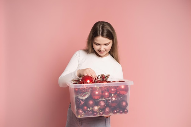 Een jong meisje houdt een doorzichtige doos met rode ballen vast om de kerstboom te versieren