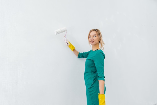 Een jong meisje houdt zich bezig met reparaties en schildert een witte muur met een roller in een nieuw appartement Renovatie van het interieur en een nieuw appartement Inwijdingsfeest en een wenselijke hypotheek