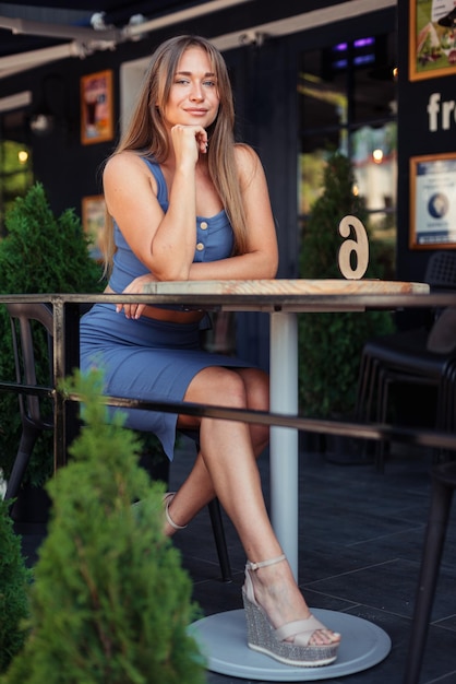 Een jong meisje in een blauwe top leunde op haar ellebogen aan een tafel in de stad in een café