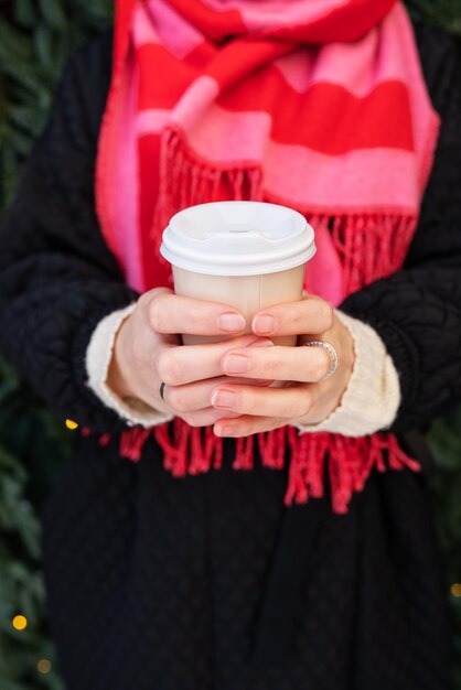Een jong meisje in een jas en een lichte sjaal houdt warme koffie in haar handen in een wegwerpbeker Koffie om te gaan wandelen
