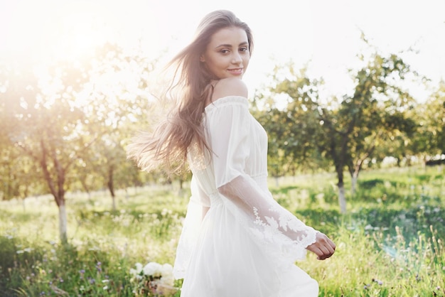 Een jong meisje in een lange witte jurk loopt in de tuin prachtige zonsondergang door de bladeren van de bomen