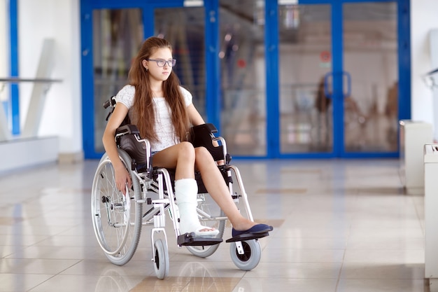 Een jong meisje in een rolstoel staat in de gang van het ziekenhuis.