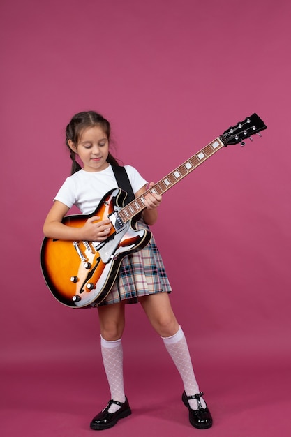 Een jong meisje in een schooluniform speelt een elektrische gitaar