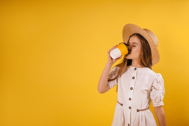 Een jong meisje in een strooien hoed drinkt koffie uit een papieren beker