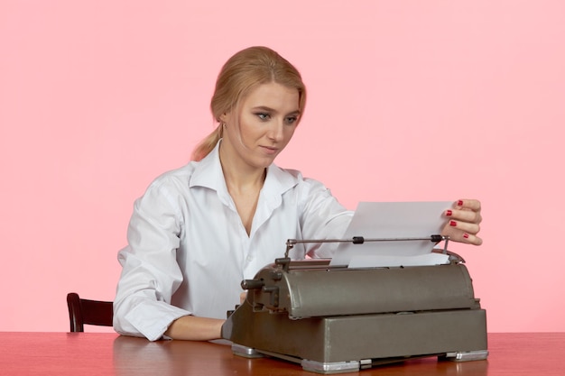 Een jong meisje in een witte blouse zit aan een bureau op kantoor en typt tekst op een retro typemachine.