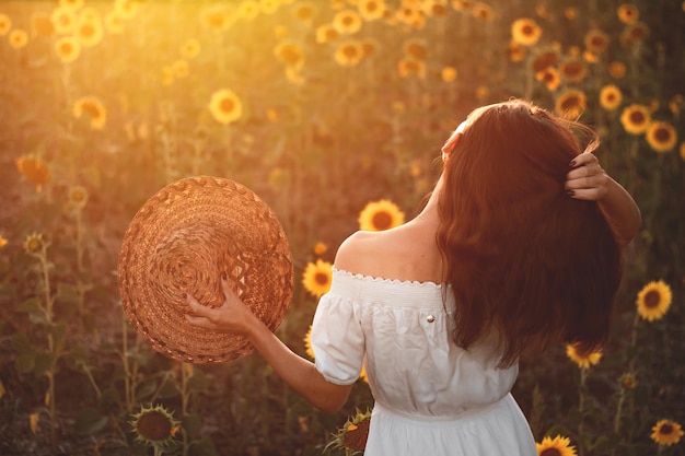 Een jong meisje in een witte jurk en hoed in een veld met zonnebloemen bij zonsondergang Portret van een vrouw met een slank figuur op een achtergrond van gele bloemen