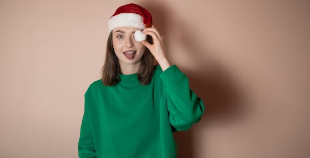 een jong meisje is gekleed in een groene trui op haar hoofd, een kerstmuts houdt haar handen in de buurt van haar gezicht en