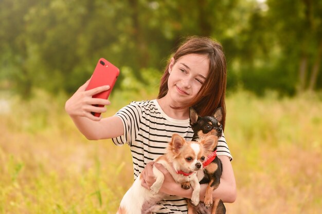 Een jong meisje maakt een selfie op een smartphone met honden in de natuur. tiener en dieren.