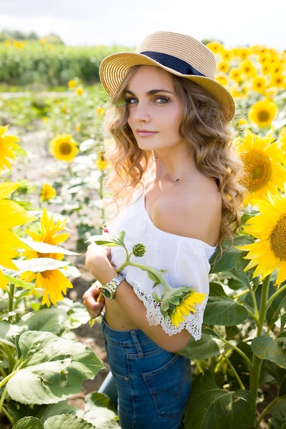 Foto een jong meisje met een model uiterlijk blond en lang haar in denim broek en een witte blouse in een zonnebloem veld