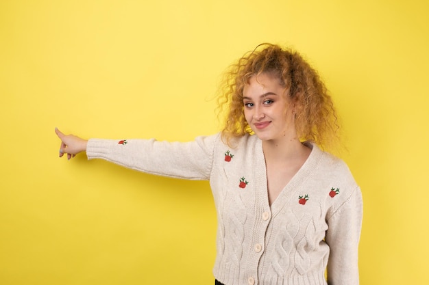 Foto een jong meisje met krullend haar wijst met een gebaar op de achtergrond van een studio.