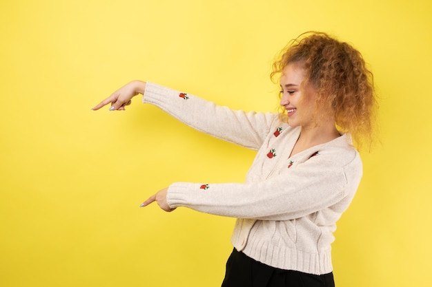 Een jong meisje met krullend haar wijst met een gebaar op de achtergrond van een studio