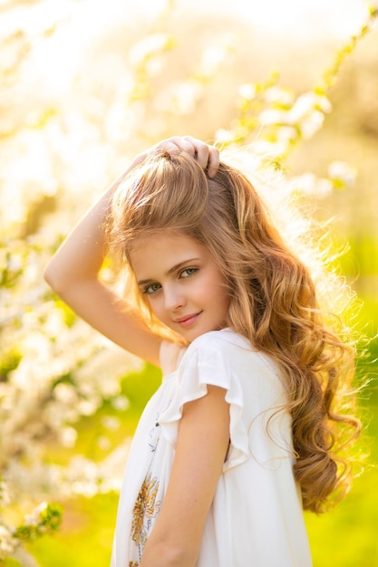 Een jong meisje met lang blond haar staat in een tuin met een bloem op de achtergrond.