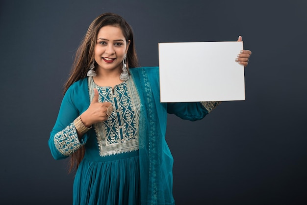 Een jong meisje of een vrouw die een traditionele Indiase jurk draagt en een uithangbord in haar handen houdt op een grijze achtergrond