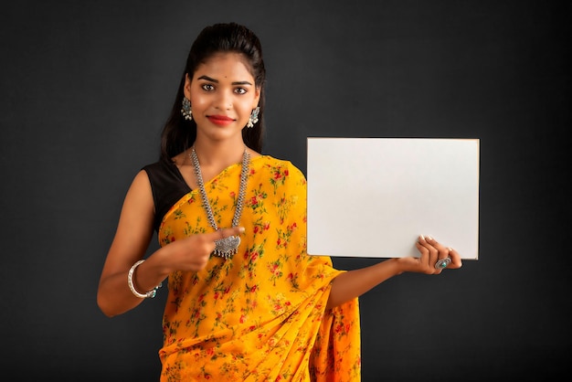 Een jong meisje of zakenvrouw die een sari draagt en een bord in haar handen houdt op een grijze achtergrond