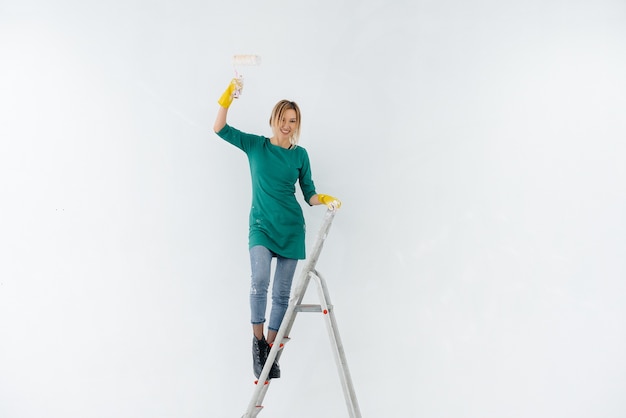 Een jong meisje op de trap schildert een witte muur met een roller. Reparatie van het interieur.