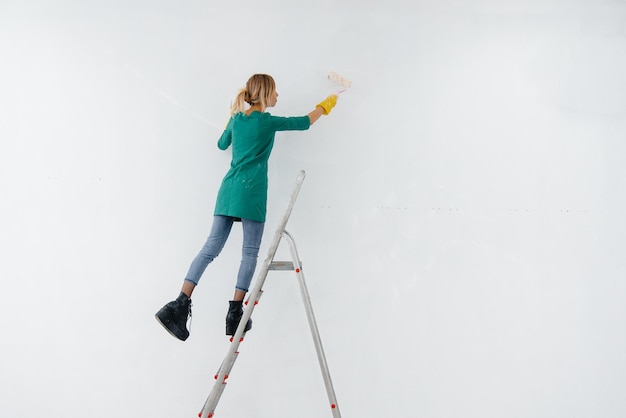 Een jong meisje op een trapladder schildert een witte muur met een roller. Reparatie van het interieur.