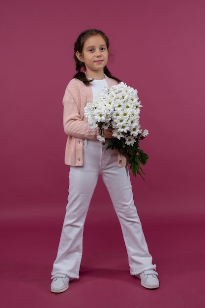 Een jong meisje poseert op een roze achtergrond met bloemen in haar handen chrysanthemum