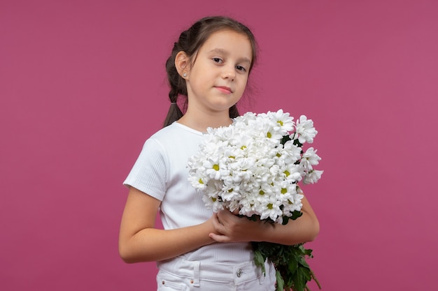 Een jong meisje poseert op een roze achtergrond met bloemen in haar handen chrysanthemum