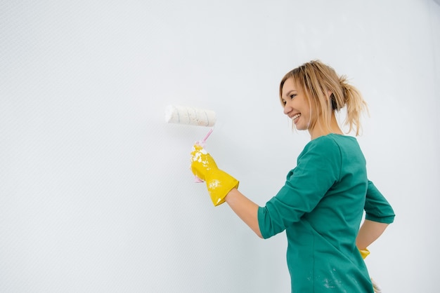 Een jong meisje schildert een witte muur met een roller. Reparatie van het interieur.