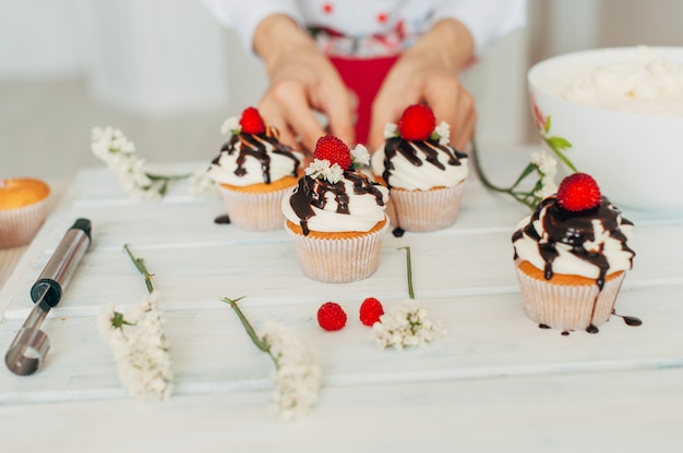 Een jong meisje siert cupcakes met verse bessen en bloemen