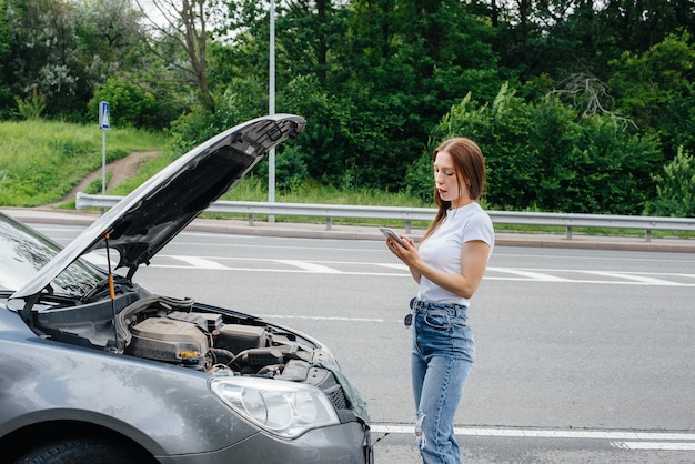 Een jong meisje staat bij een kapotte auto midden op de snelweg en belt om hulp aan de telefoon. Storing en pech van de auto. Wachten op hulp.