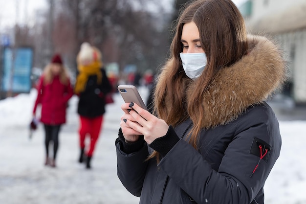 Een jong meisje staat in de buurt van de weg en schrijft een bericht op de smartphone met een medisch masker Bescherming tegen virusuitbraken griep en luchtvervuiling door auto's in de stad