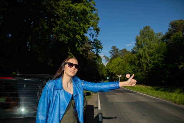 Een jong meisje staat op de weg in een groen bos naast een gebroken auto en vraagt om hulp om andere auto's te stoppen