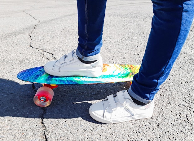 Een jong meisje staat op een kleurrijk pennyboard in de stad, asfaltweg. Gezonde levensstijl, jeugd, tiener, kind, sport, skateboard, actief, entertainment. Zijaanzicht van voeten en plank, close-up