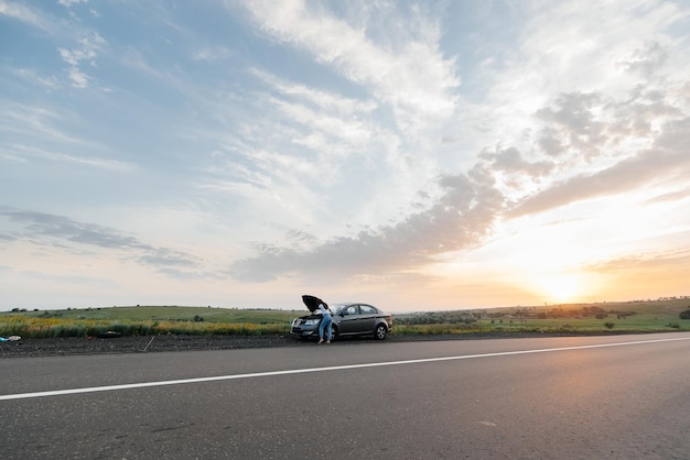 Een jong meisje staat tijdens zonsondergang in de buurt van een auto met pech midden op de snelweg en probeert telefonisch om hulp te bellen Wachten op hulp Autoservice Autopech onderweg