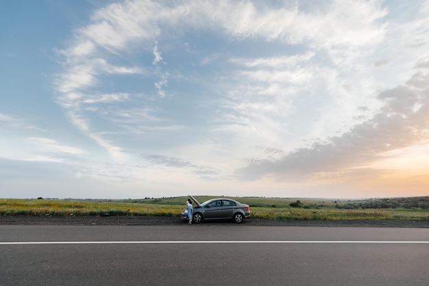 Een jong meisje staat tijdens zonsondergang in de buurt van een auto met pech midden op de snelweg en probeert telefonisch om hulp te bellen Wachten op hulp Autoservice Autopech onderweg