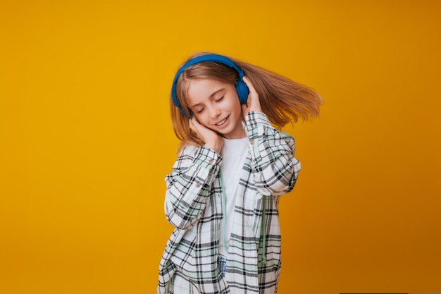 Een jong meisje van 1113 jaar oud met koptelefoon luistert naar muziek en danst in de studio op een gele achtergrond